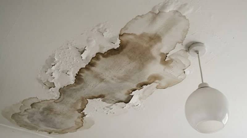 Water-stained and discoloured ceiling in an apartment directly below a bathroom, showing a shower leak from the unit above