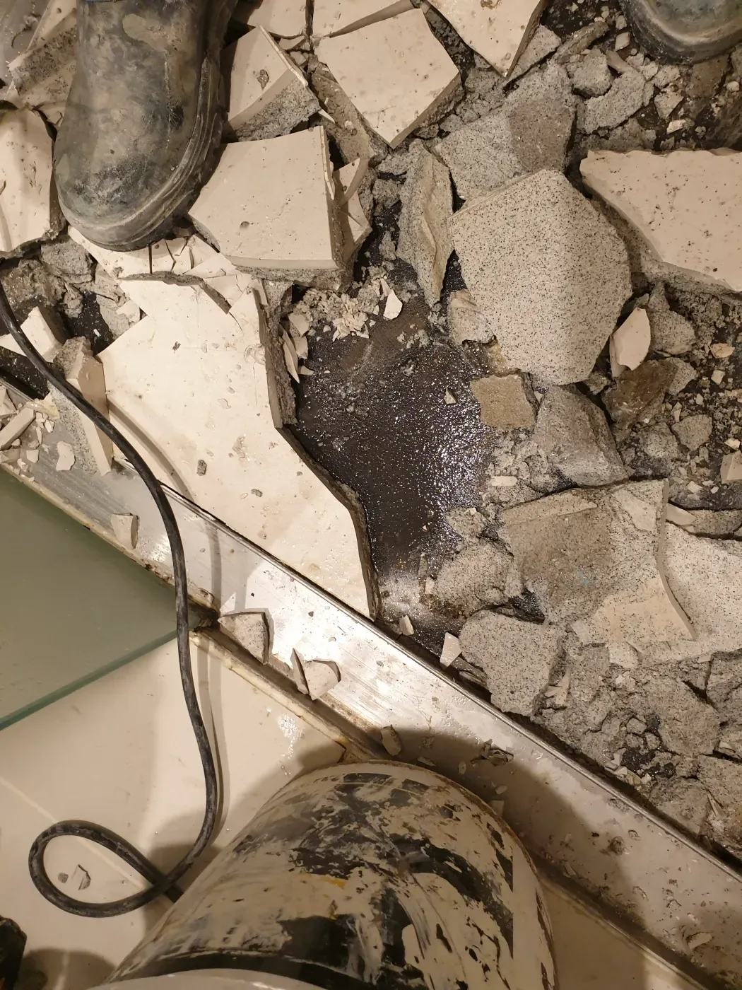 Demolished bathroom floor showing debris and services below