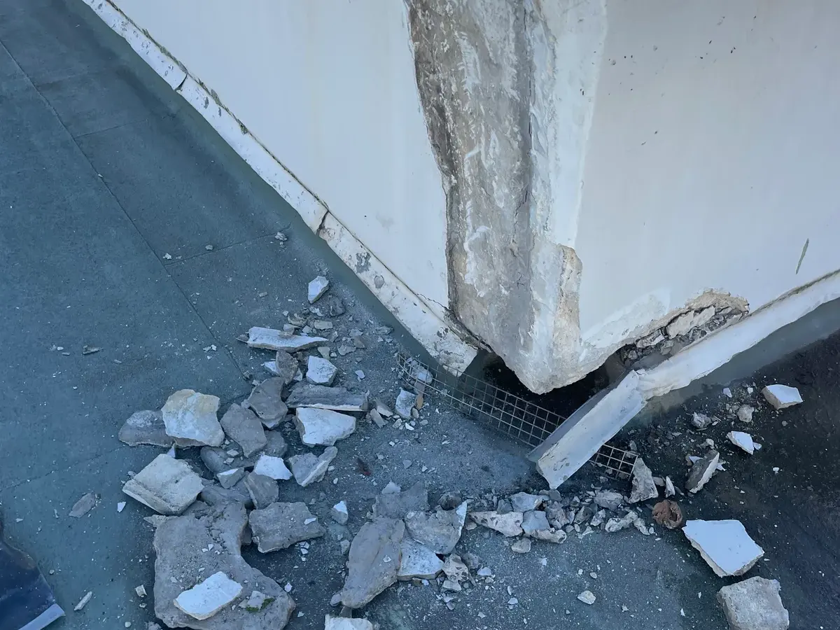 Rendered parapet broken out at the corner exposing the reinforcement behind it, with the spalled material cleared onto the roof deck